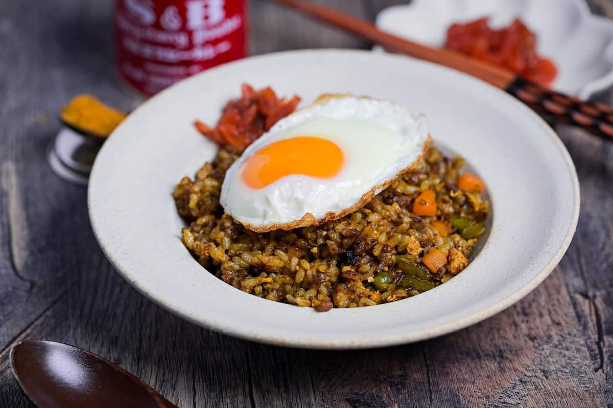 A white bowl of curry fried rice topped with a fried egg and some Japanese curry pickles (fukujinzuke) side view