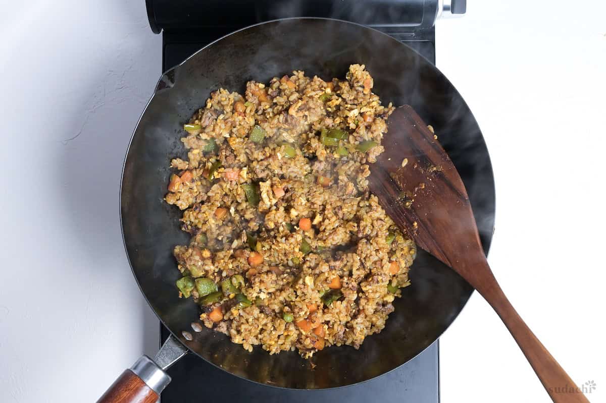 Japanese style curry fried rice in a wok with a dark wooden spatula
