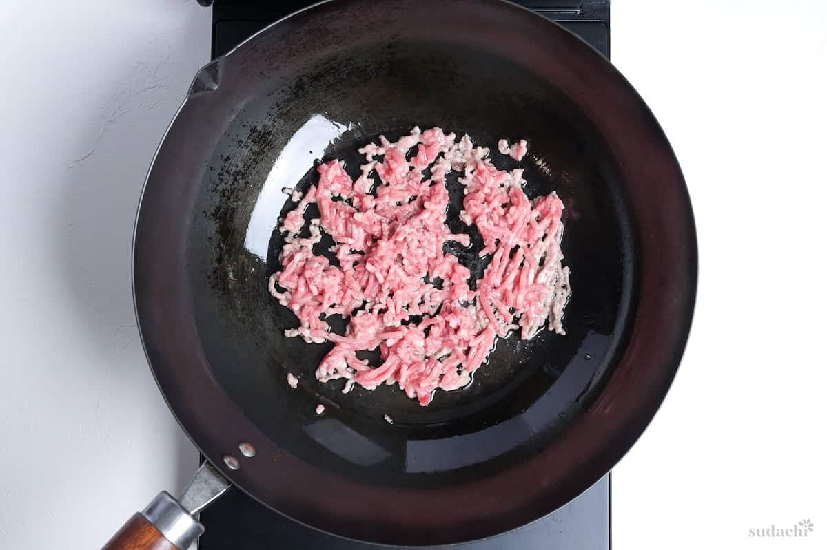 Ground pork frying in a wok on the stove top