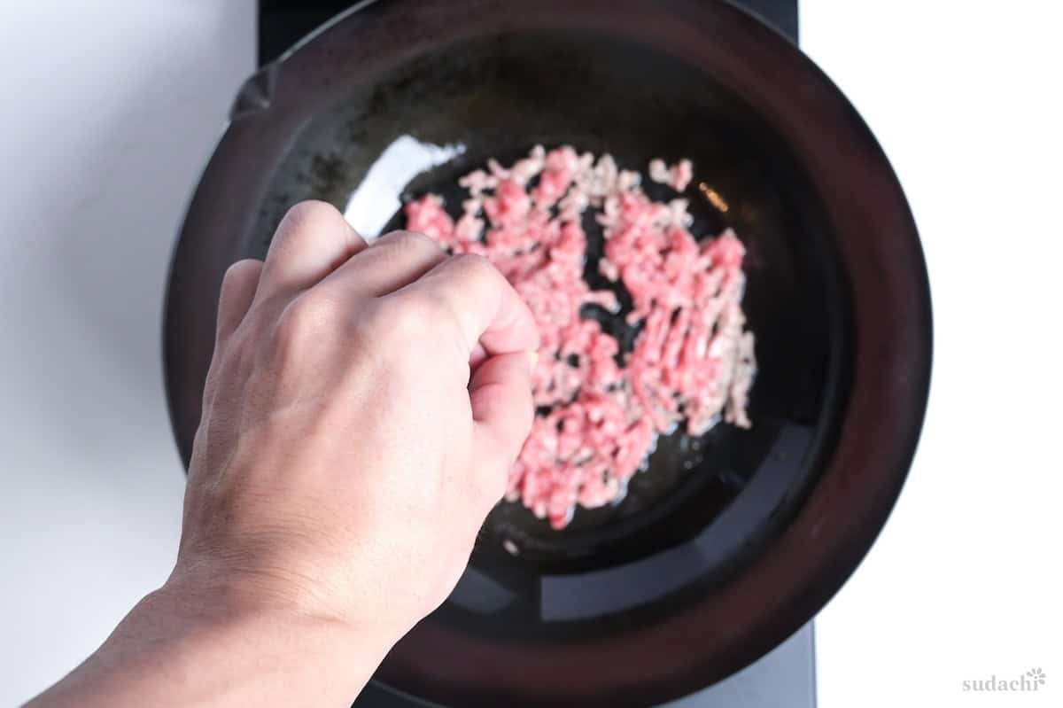 Seasoning ground pork in a wok on the stove top