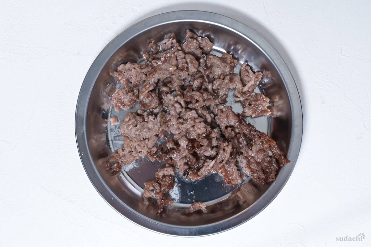 Browned ground pork on a steel plate on a white background