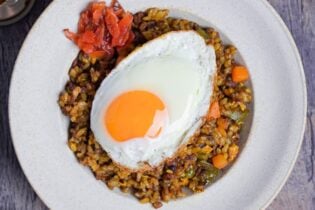 A white bowl of curry fried rice topped with a fried egg and some Japanese curry pickles (fukujinzuke) thumb