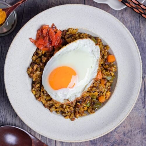 A white bowl of curry fried rice topped with a fried egg and some Japanese curry pickles (fukujinzuke) thumb