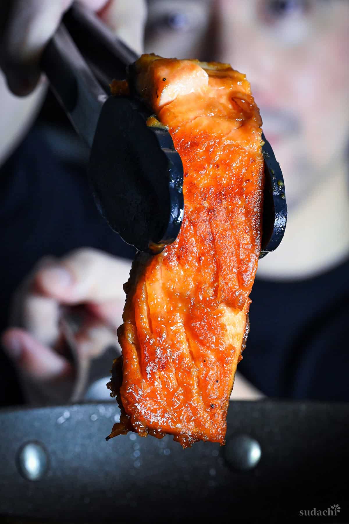 Yuto Omura holding a piece of miso glazed salmon with cooking tongs