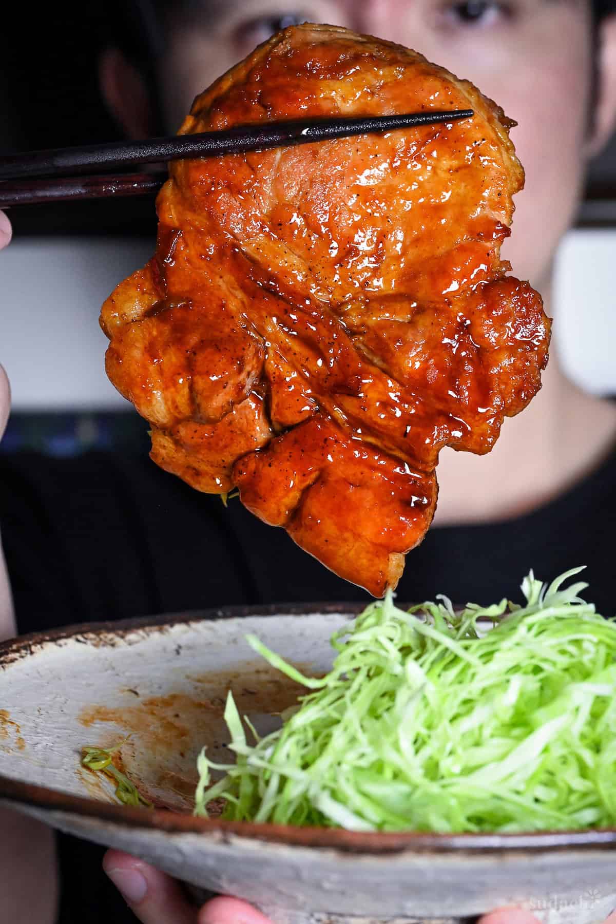 Yuto Omura holding up a whole tonteki pork steak with dark brown chopsticks