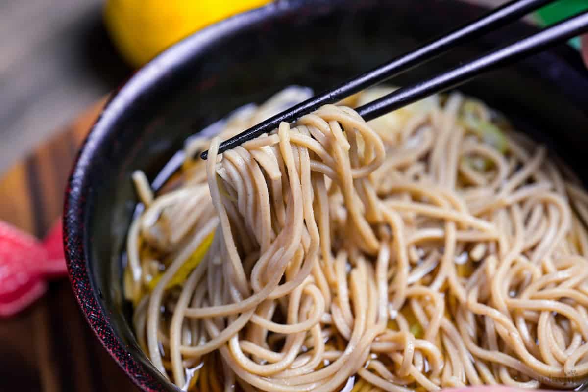 Close up of soba noodles held up with black chopsticks