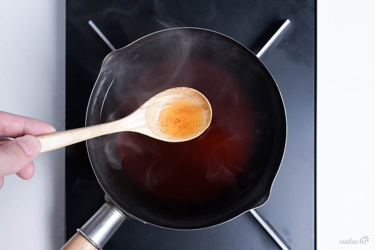 Kake soba soup on a wooden spoon held above the pan for taste testing