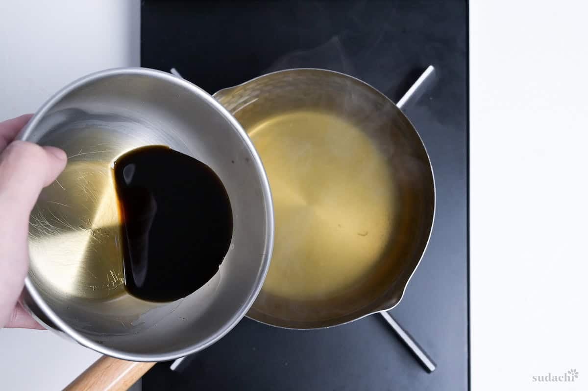 Pouring concentrated kake noodle soup base into dashi broth in a Japanese yukihira pot on the stove top