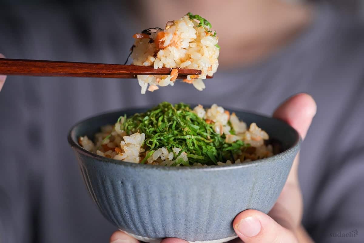 Yuto Omura holding up a scoop of salmon maze gohan with wooden chopsticks over a gray Japanese rice bowl