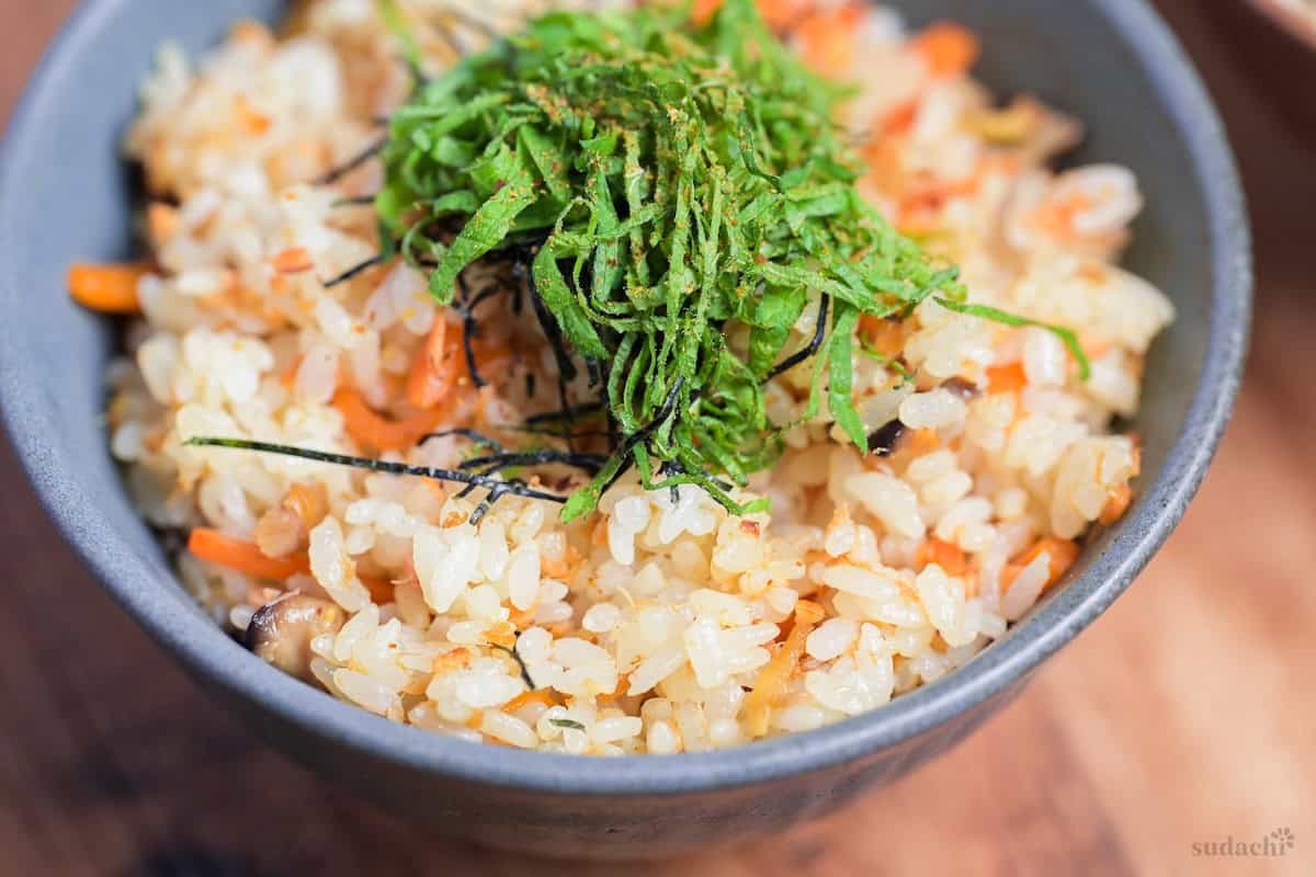 Salmon Maze Gohan topped with shredded nori and shiso leaves in a gray ceramic Japanese rice bowl