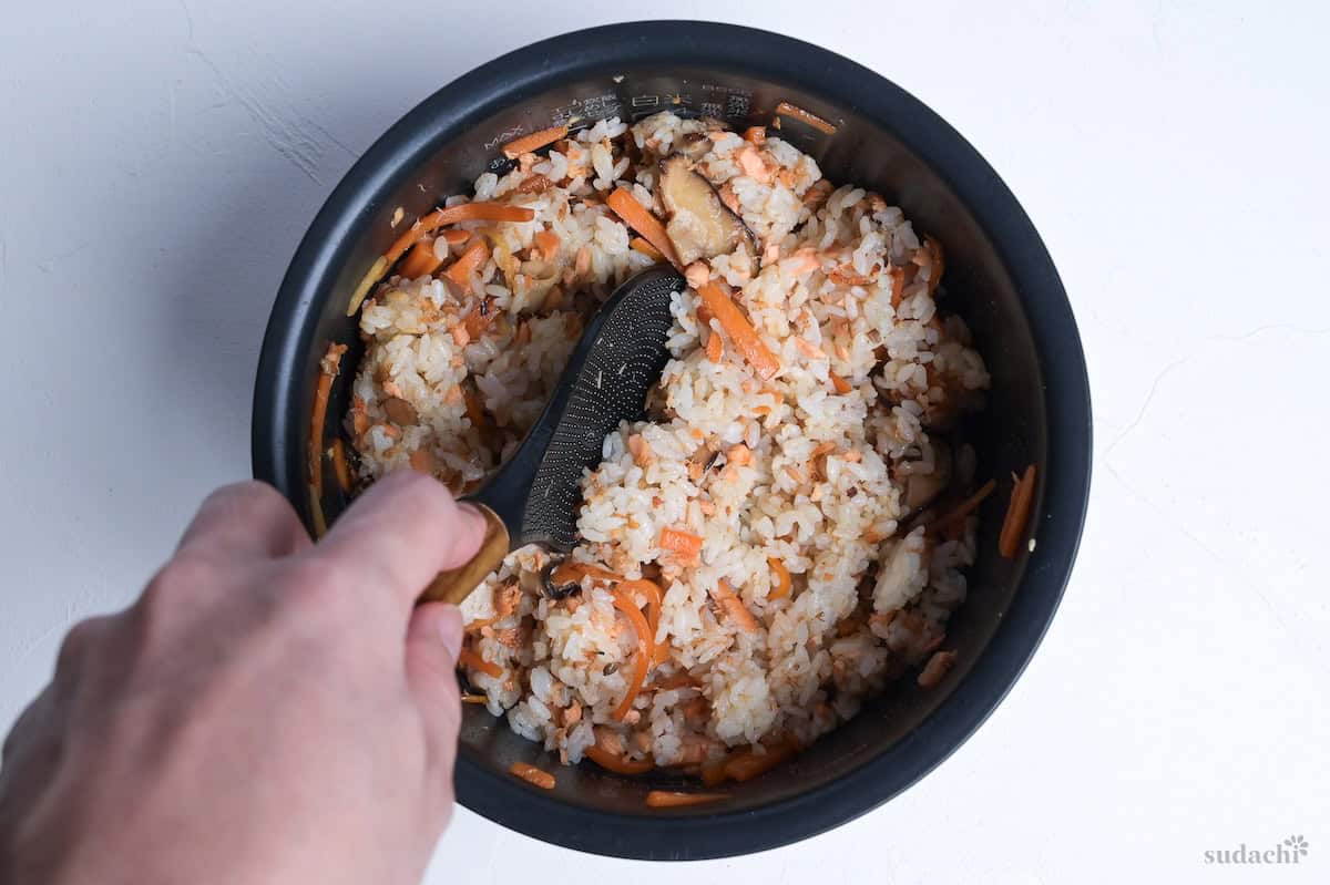 flavored pan-fried salmon and vegetables mixed with rice in a black rice cooker pot