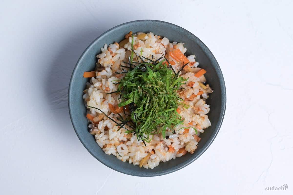 Salmon maze gohan topped with shredded nori and shiso leaves on a white background