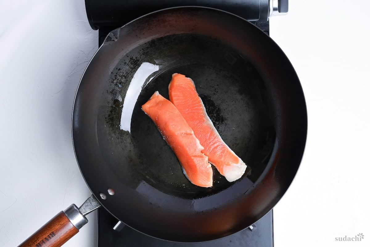 two salmon fillets frying in a wok on the stove top