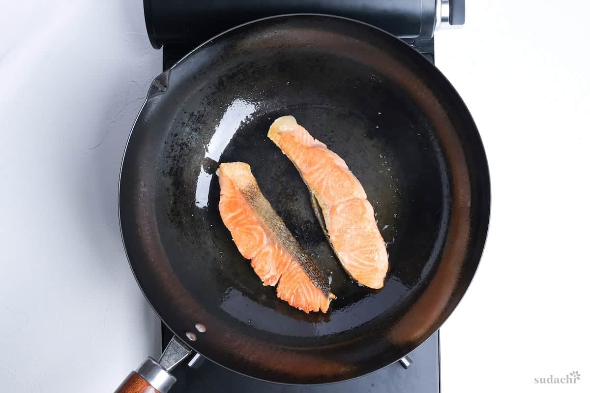 two salmon fillets frying in a wok on the stove top