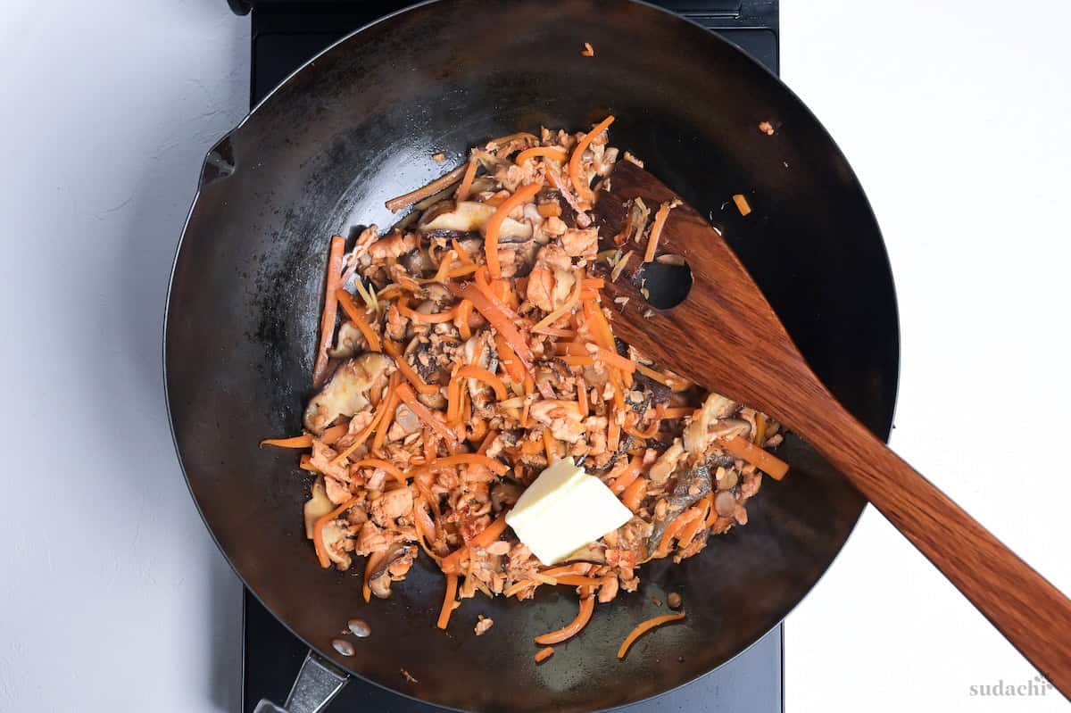 melting butter over ingredients for salmon maze gohan in a wok