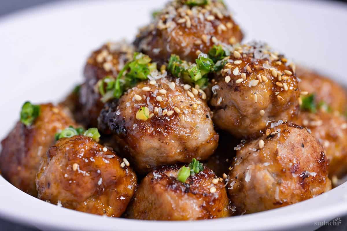 Teriyaki meatballs stacked in a pyramid on a white dish and topped with sesame seeds, chopped green onions and grated parmesan cheese