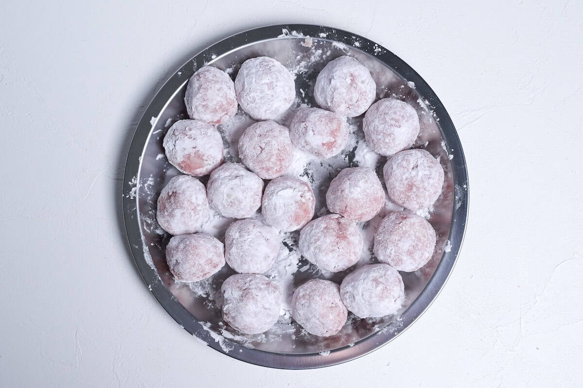 raw ground pork meatballs coated with starch on a steel prep plate