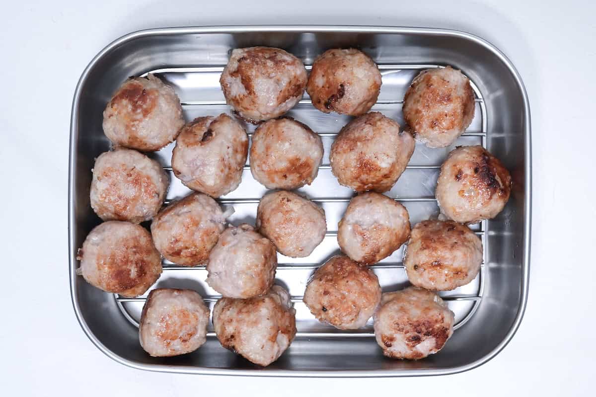 cooked pork meatballs resting on a wire rack in a steel container