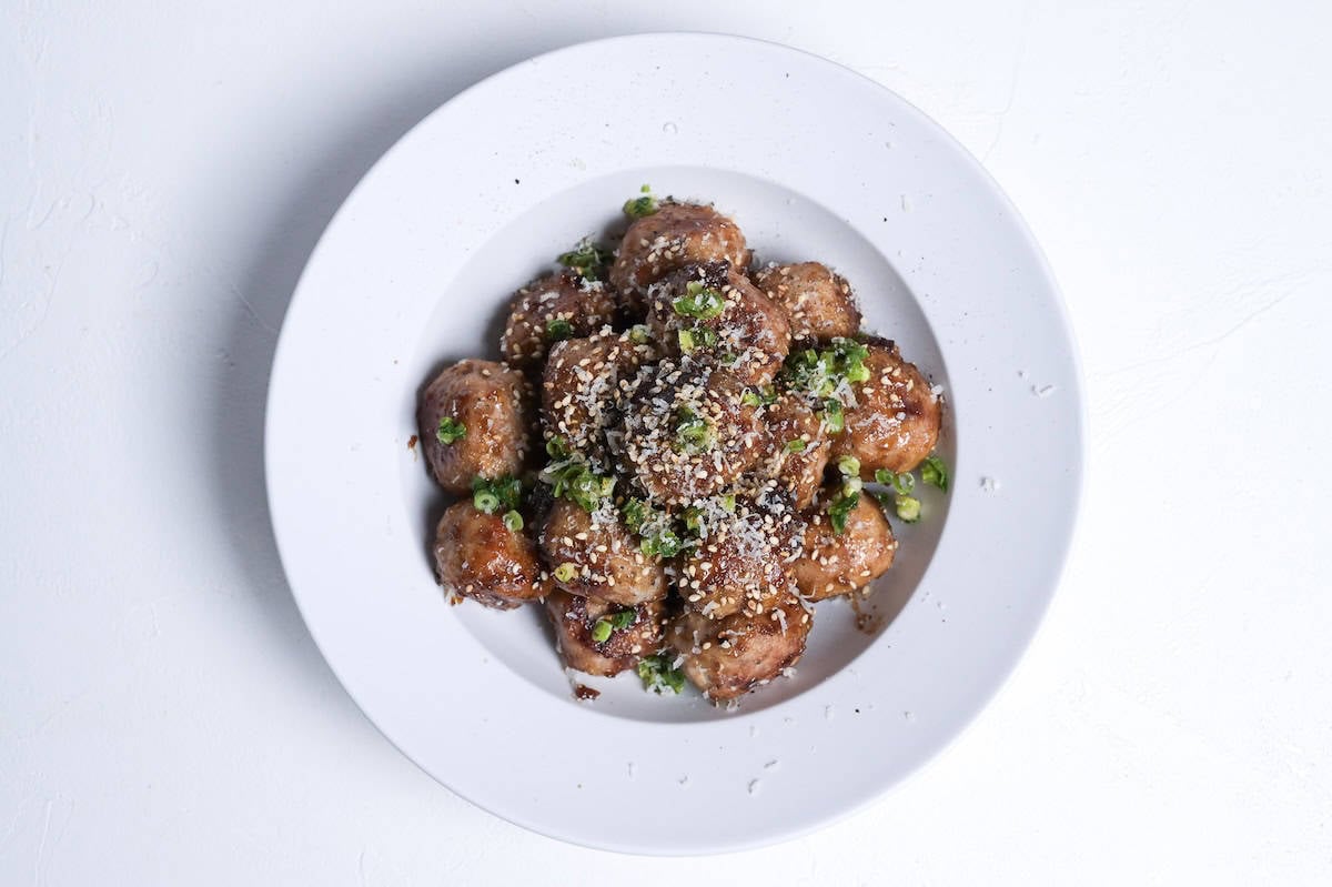 pork teriyaki meatballs stacked in a dish and topped with grated parmesan, sesame seeds and chopped green onions