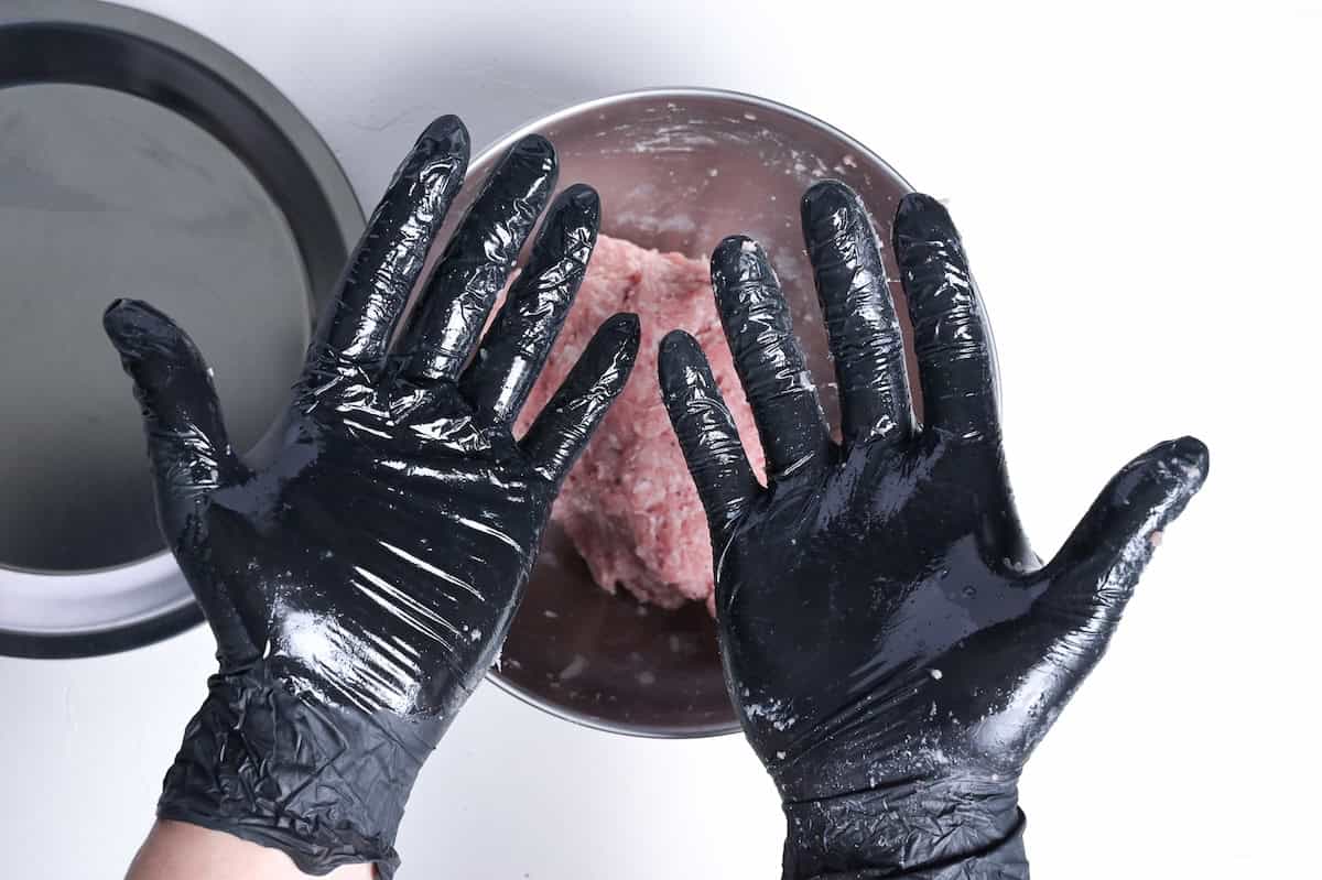 two hands wearing black food-safe gloves sprayed with oil to shape meatballs