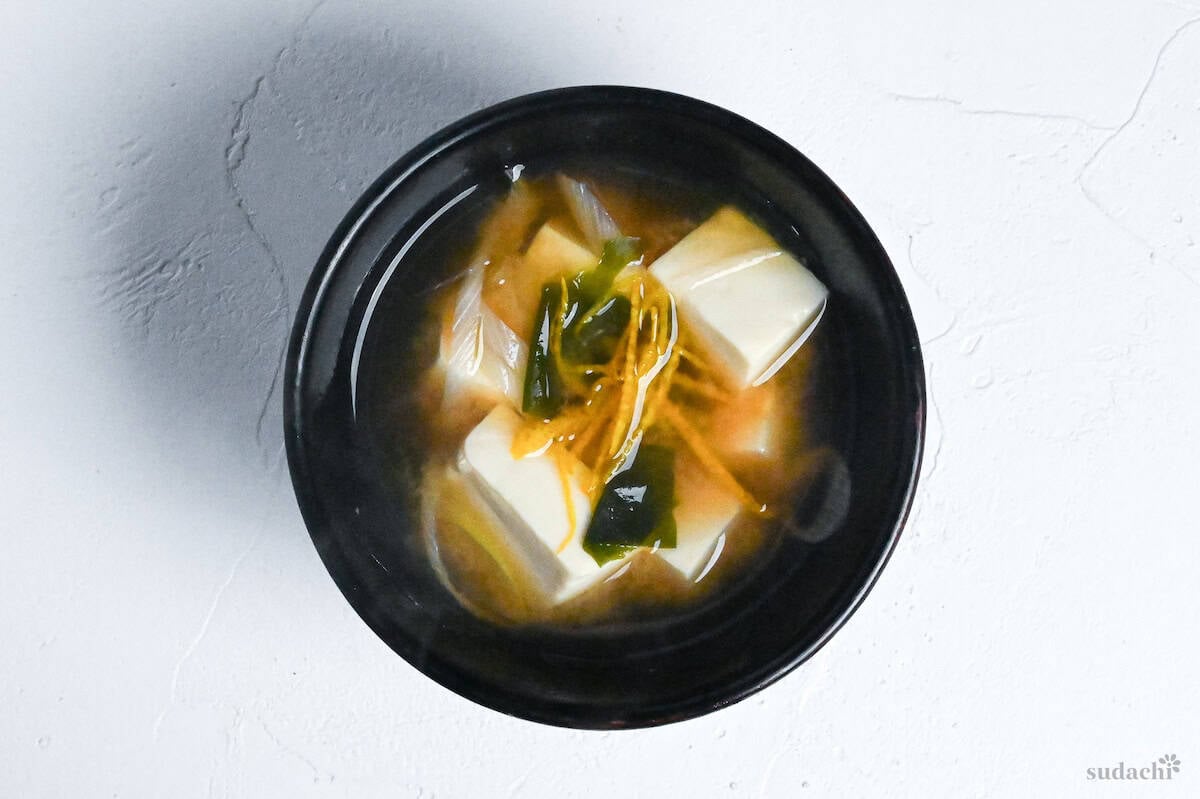 Japanese tofu miso soup with yuzu peel in a black bowl on a white background