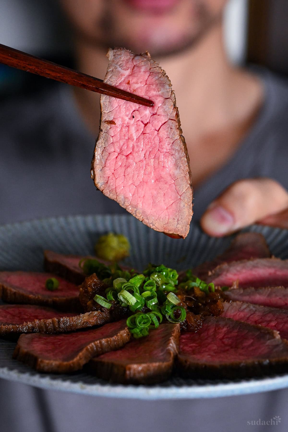 Yuto Omura holding a piece of Wafu Roast Beef with wooden chopsticks