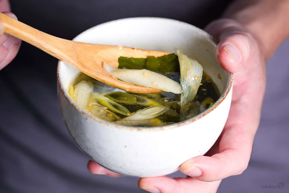 Yuto Omura holding a bowl of wakame soup with some wakame and Japanese leeks scooped onto a wooden spoon