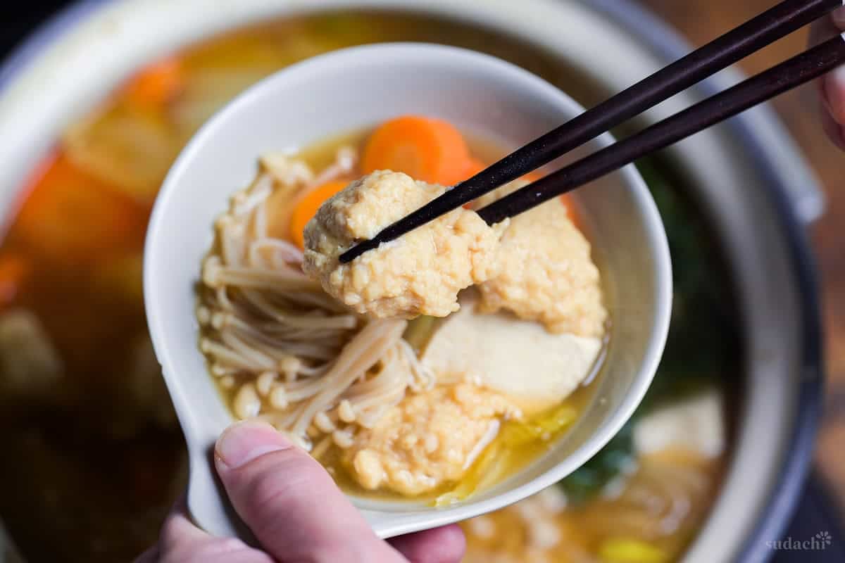 Chicken meatballs from chanko nabe held up with black chopsticks