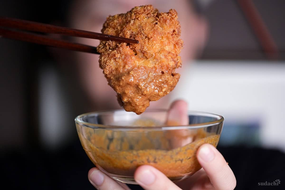 Yuto Omura holding a piece of chicken katsu with wooden chopsticks, dipped in homemade sesame katsu sauce