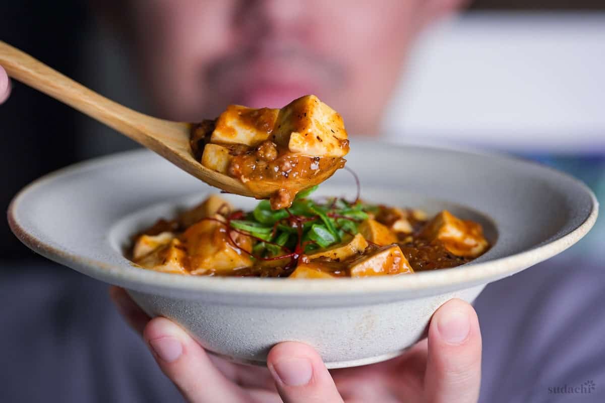 Yuto Omura holding up a wooden spoonful of Japanese style mapo tofu (mabo dofu) over a bowl