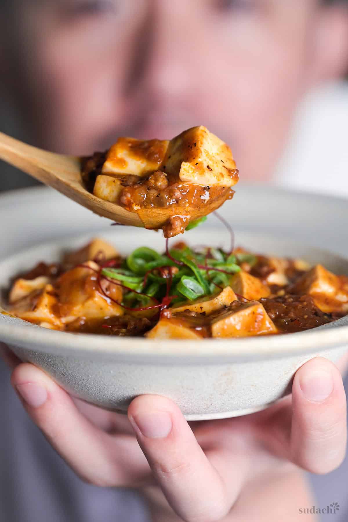 Yuto Omura holding up a wooden spoonful of Japanese style mapo tofu (mabo dofu) over a bowl