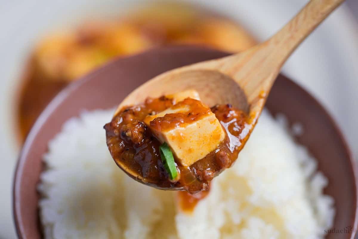 Close up of Japanese mapo tofu on a light wooden spoon above a bowl of rice