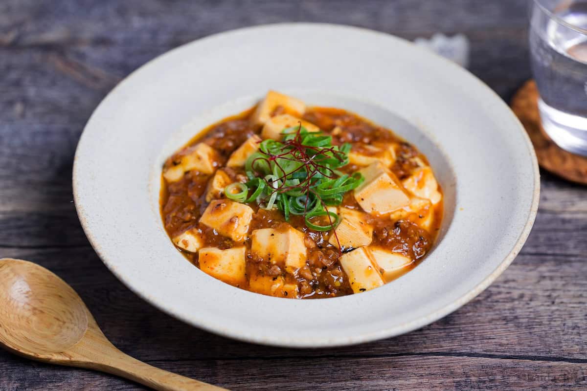 Japanese style mapo tofu in a cream dish topped with chopped green onions and red chili threads
