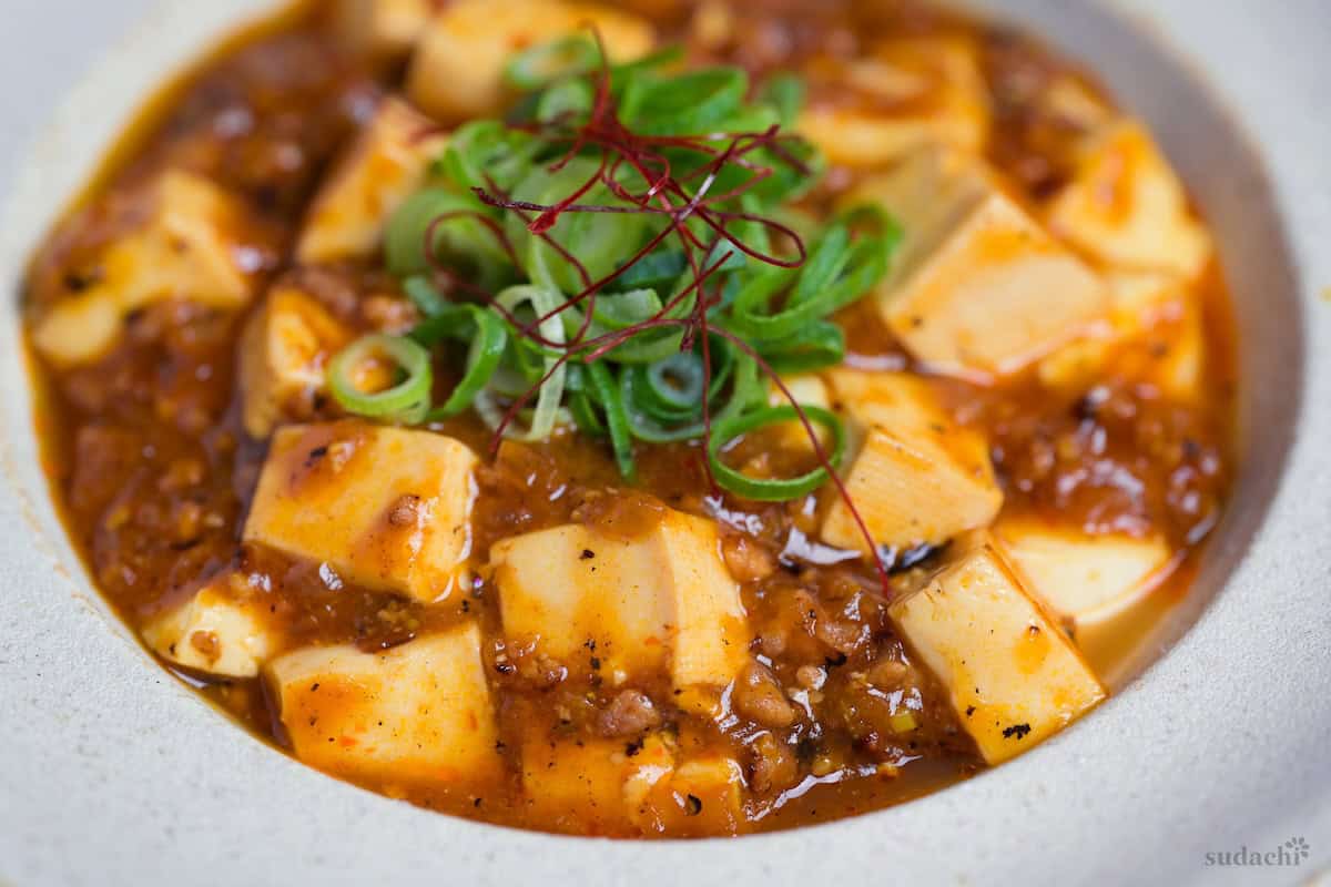 Close up of Japanese style mapo tofu in a cream dish topped with chopped green onions and red chili threads