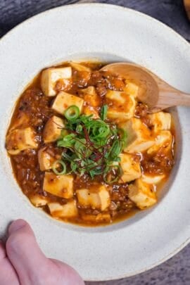 Japanese mapo tofu (mabo dofu) being scooped onto a light wooden spoon from a cream colored bowl