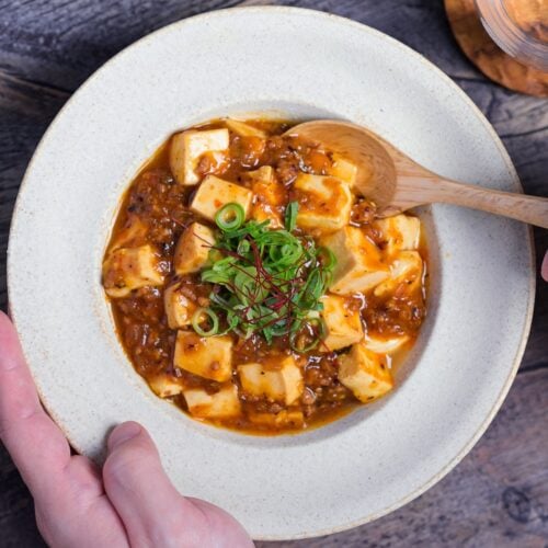 Japanese mapo tofu (mabo dofu) being scooped onto a light wooden spoon from a cream colored bowl
