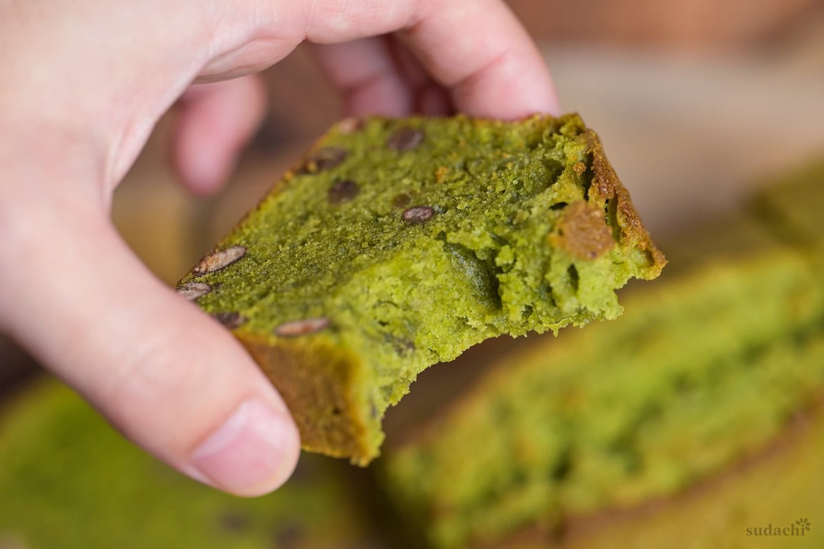 A hand holding a slice of matcha and adzuki bean pound cake with a bite missing