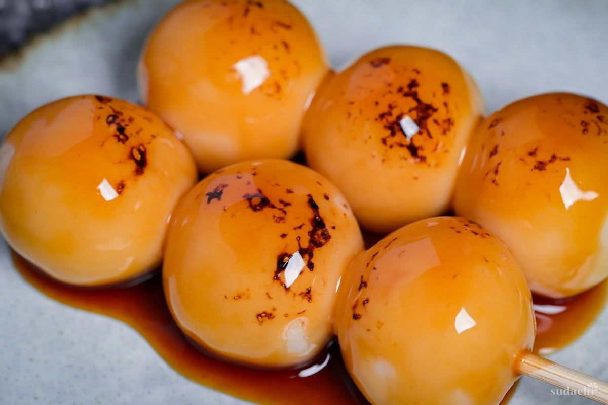 Two homemade tofu mitarashi dango on an off-white plate with brown rim