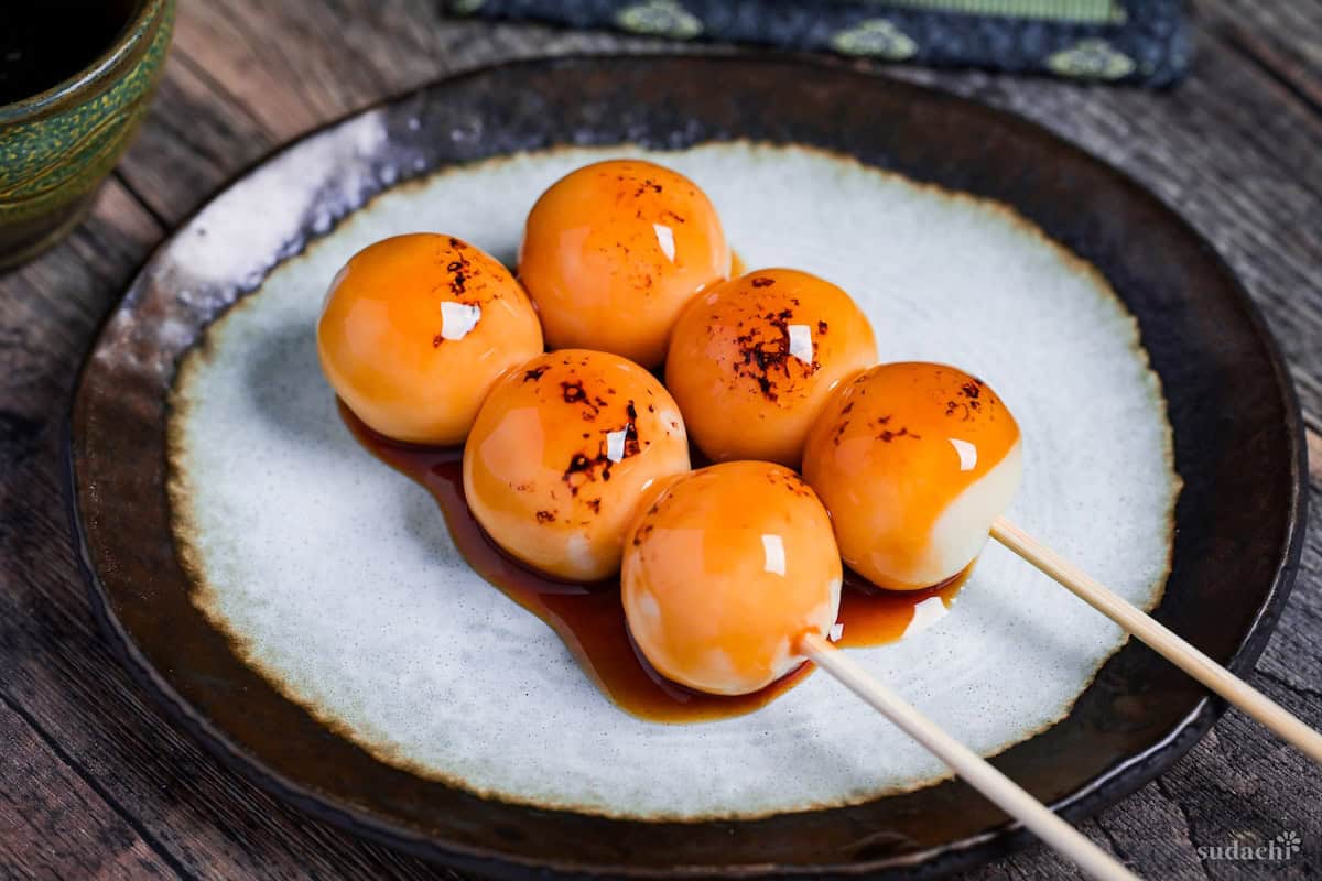 Two homemade tofu mitarashi dango on an off-white plate with brown rim