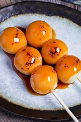 Two homemade tofu mitarashi dango on an off-white plate with brown rim