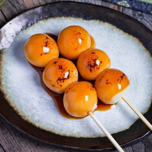 Two homemade tofu mitarashi dango on an off-white plate with brown rim