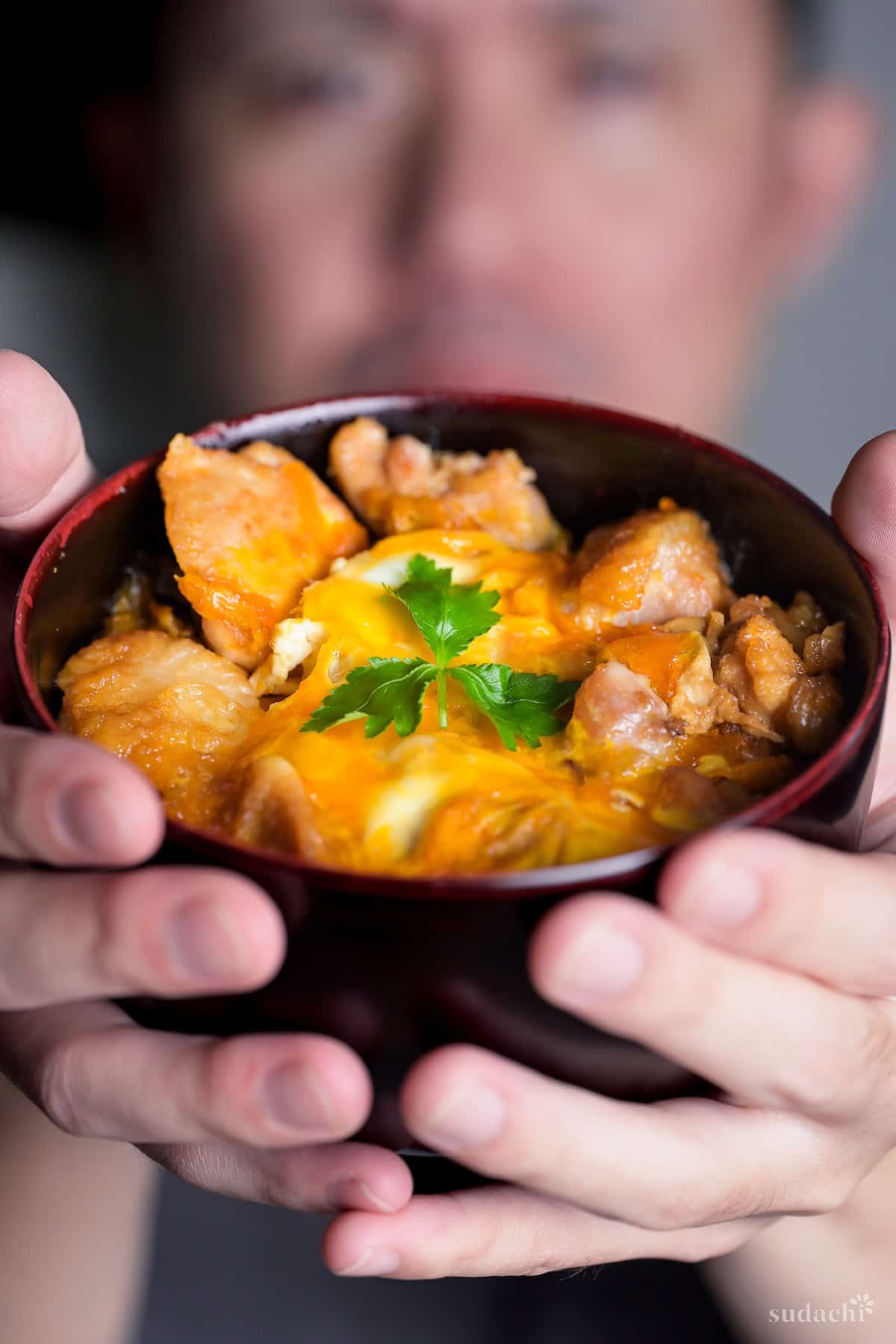 Yuto Omura holding up a bowl of Oyakodon topped with a piece of mitsuba (Japanese parsley)