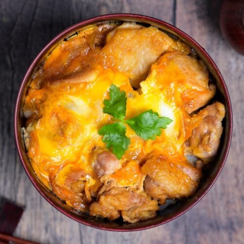 A bowl of Oyakodon topped with a piece of mitsuba (Japanese parsley) top down view