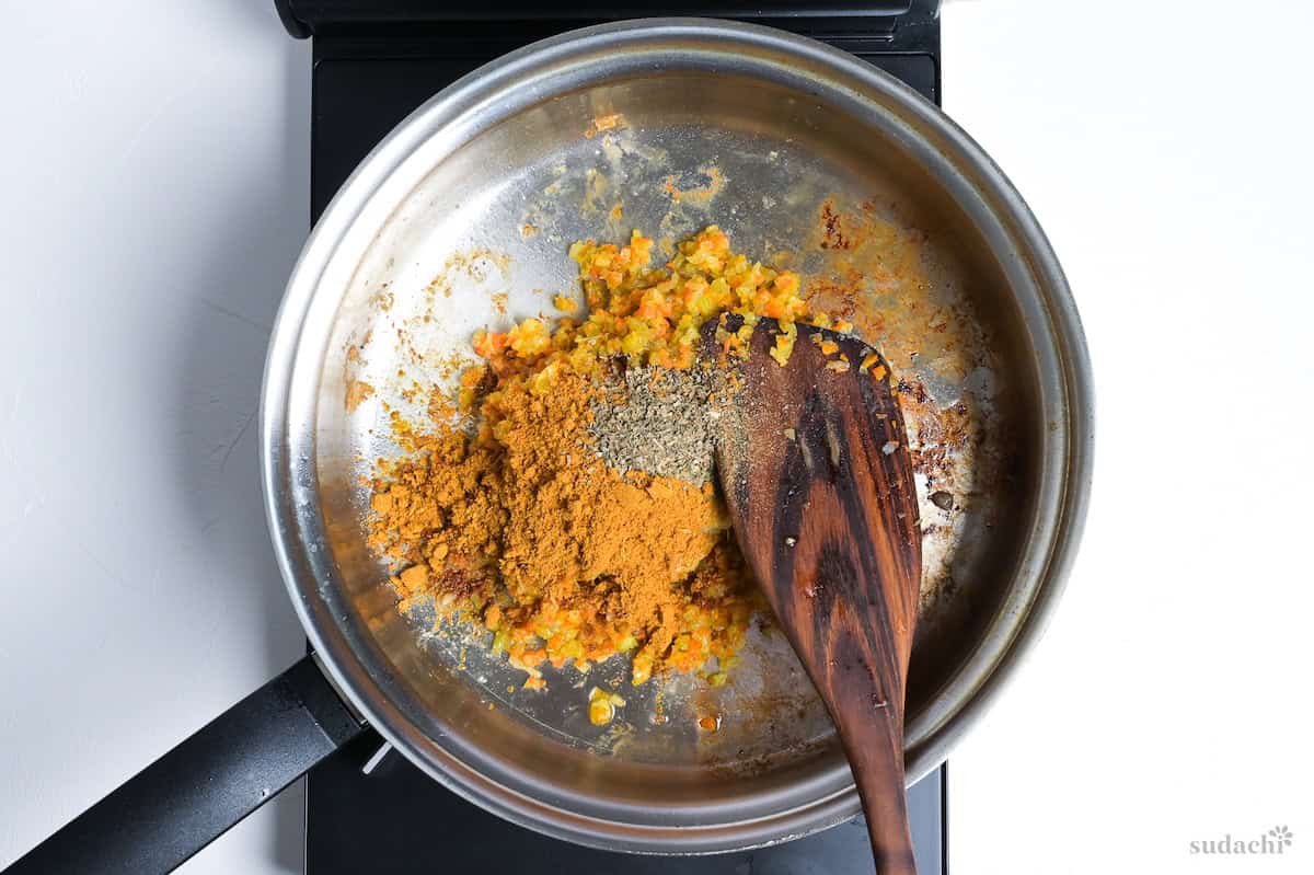 Curry powder and herbs mixed into Soffrito in a stainless steel pan on the stove top