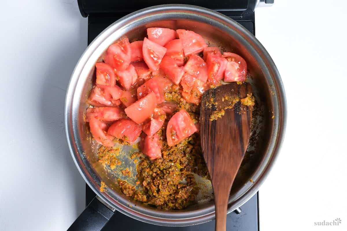 cut tomatoes and curry infused Soffrito in a stainless steel pan on the stove top