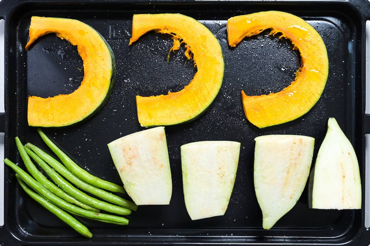 Kabocha squash slices, whole French beans and quartered Japanese eggplant on a baking sheet spritzed with oil