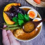 Japanese Soup Curry topped with oven roasted vegetables, boiled eggs and a celery leaf in a cream bowl