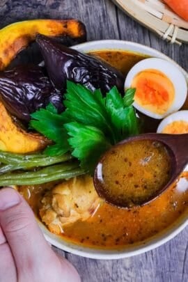 Japanese Soup Curry topped with oven roasted vegetables, boiled eggs and a celery leaf in a cream bowl