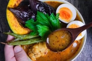 Japanese Soup Curry topped with oven roasted vegetables, boiled eggs and a celery leaf in a cream bowl