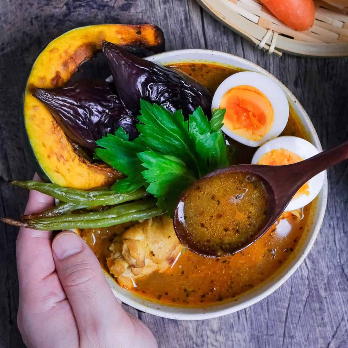Japanese Soup Curry topped with oven roasted vegetables, boiled eggs and a celery leaf in a cream bowl